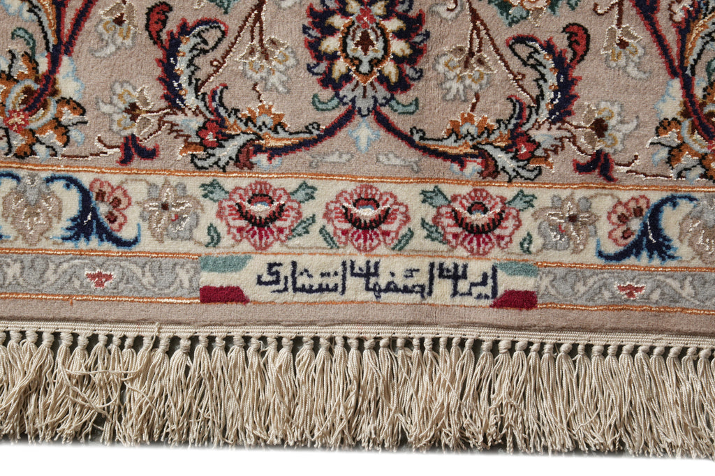 Close-up of an ornate patterned rug with cream, beige, red, blue, and green floral motifs, a decorative border, and tasseled fringe along the bottom edge.