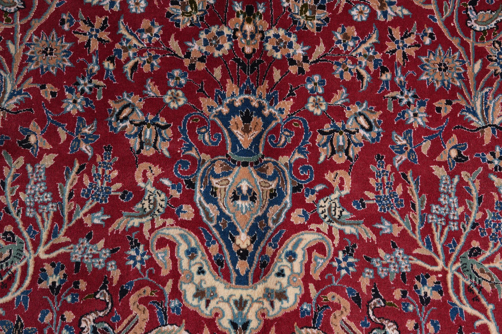 A close-up of an ornate red patterned rug with a central floral and scroll motif in blue, beige, and cream tones.