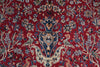 Load image into Gallery viewer, A close-up of an ornate red patterned rug with a central floral and scroll motif in blue, beige, and cream tones.