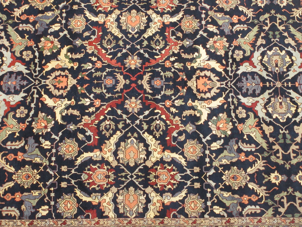 A close-up of an ornate traditional patterned rug with a dark navy blue background and intricate floral motifs in beige, red, orange, and muted green.
