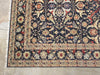 Load image into Gallery viewer, A traditional oriental area rug with a dark navy blue field, intricate floral motifs in beige, red, and gold, and a detailed multi-colored border, shown laid out on a light concrete floor.