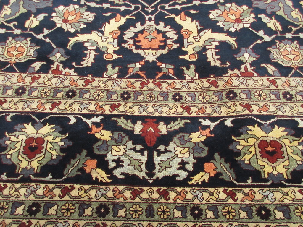 A close-up of an ornate traditional rug with a dark navy blue field, cream borders, and floral motifs in red, orange, green, and beige.