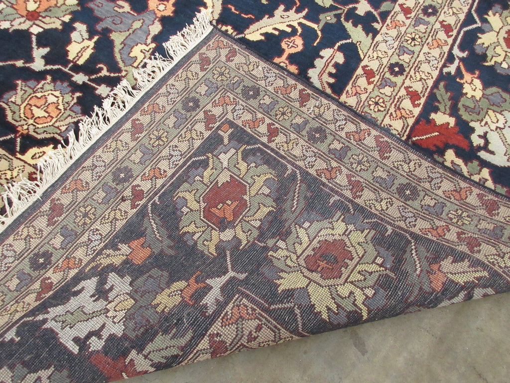 A close-up of a patterned area rug corner showing a dark navy field, cream and rust floral medallion, and a beige border, with white fringe visible along one edge.