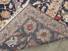 Load image into Gallery viewer, A close-up of a patterned area rug corner showing a dark navy field, cream and rust floral medallion, and a beige border, with white fringe visible along one edge.