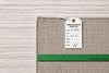 Load image into Gallery viewer, A close-up of a woven rug corner with a white product tag attached and a green measuring ruler along the edge, showing the rug texture and dimensions against a matching rug background.