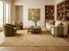 Load image into Gallery viewer, A large beige patterned area rug covers a hardwood floor in a styled living room with a cream sofa, olive green armchairs, a wooden coffee table, and built-in wooden bookshelves.