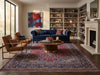 Load image into Gallery viewer, A styled living room featuring a deep blue tufted sofa, two brown armchairs with gold frames, a round wooden coffee table, a large red and blue patterned oriental rug, and built-in bookshelves beside a fireplace.