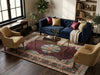 Load image into Gallery viewer, A styled living room scene featuring a deep blue velvet sofa with burgundy and beige pillows, flanked by two tan armchairs on a large ornate patterned area rug. A glass-top coffee table sits in the center, with a bookshelf and window in the background.