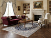 Load image into Gallery viewer, A classic living room scene featuring a large navy blue and beige patterned area rug on a dark wood herringbone floor. 