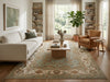 Load image into Gallery viewer, A styled living room featuring a large traditional-style area rug in beige, blue, and rust tones, a cream sofa, a tan armchair, a wooden coffee table, and tall windows with sheer curtains.