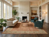 Load image into Gallery viewer, A styled living room featuring a large traditional-style area rug in warm beige and rust tones, with a cream sofa, two teal armchairs, a wooden coffee table, and a white fireplace in the background.