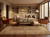Load image into Gallery viewer, A styled living room featuring a large beige patterned area rug under a dark wood coffee table, flanked by two brown leather armchairs and a light beige sofa, set against a built-in wood bookshelf wall.
