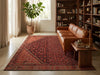 Load image into Gallery viewer, A large traditional-style area rug in deep red and brown tones is styled in a cozy, sunlit living room with a brown leather sofa, wooden bookshelves, and a potted plant.