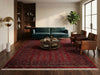 Load image into Gallery viewer, A large red and navy patterned area rug with fringe, styled in a modern living room with a teal sofa, brown leather armchairs, a round coffee table, and a gold floor lamp.