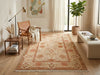 Load image into Gallery viewer, A rectangular area rug with a traditional floral pattern in beige, rust, and terracotta tones, styled in a bright, modern living room with a leather armchair, side table, and potted plant.
