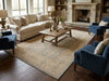 Load image into Gallery viewer, A large beige and blue traditional-style area rug in a styled living room with a cream sofa, blue armchairs, a wooden coffee table, and a stone fireplace.