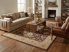 Load image into Gallery viewer, A styled living room featuring a large rectangular area rug with a traditional floral pattern in beige and brown, placed under a rustic wooden coffee table. The room includes a beige sofa, a brown leather armchair, a wooden coffee table, and a fireplace in the background.