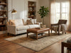 Load image into Gallery viewer, A styled living room featuring a cream-colored sofa, a brown leather ottoman, a brown armchair with a beige throw, and a large beige patterned area rug on a hardwood floor.
