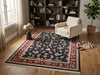 Load image into Gallery viewer, A traditional oriental area rug with a navy blue field, red border, and beige floral motifs, styled in a warm, modern living room with a cream armchair, wooden bookshelves, and a potted plant.