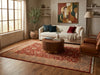 Load image into Gallery viewer, A styled living room featuring a large traditional-style area rug with a red and beige floral pattern on a hardwood floor. The room is furnished with a cream-colored sofa, a round wooden coffee table, a brown leather armchair, and a potted tree.