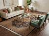 Load image into Gallery viewer, A styled living room featuring a large traditional-style area rug with a central medallion pattern in beige, rust, and navy. The rug is styled with a cream sofa, two green velvet armchairs, a glass-top coffee table with a gold frame, and potted plants on dark wood floors.
