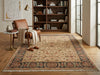 Load image into Gallery viewer, A large traditional area rug with an intricate floral pattern in beige, rust, and navy, styled in a warm, modern living room next to a brown leather armchair and a wooden bookshelf.