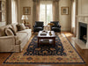 Load image into Gallery viewer, A large traditional oriental area rug in navy blue, beige, and gold tones, styled in a classic living room with a beige sofa, dark leather armchairs, a wooden coffee table, and a fireplace.