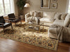 Load image into Gallery viewer, A large traditional-style area rug with an ornate floral pattern in beige, brown, and muted blue tones, styled in a cozy living room with a cream sectional sofa, glass coffee table, and dark leather armchairs.