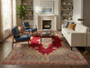 Load image into Gallery viewer, A large traditional Persian-style area rug in red, beige, and blue tones, styled in a bright living room with a white sofa, blue armchairs, a wooden coffee table, and a fireplace in the background.