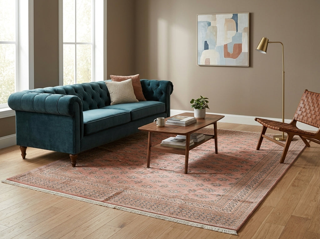 A teal velvet tufted loveseat sofa in a styled living room setting with a pink patterned area rug, wooden coffee table, and a modern woven chair.