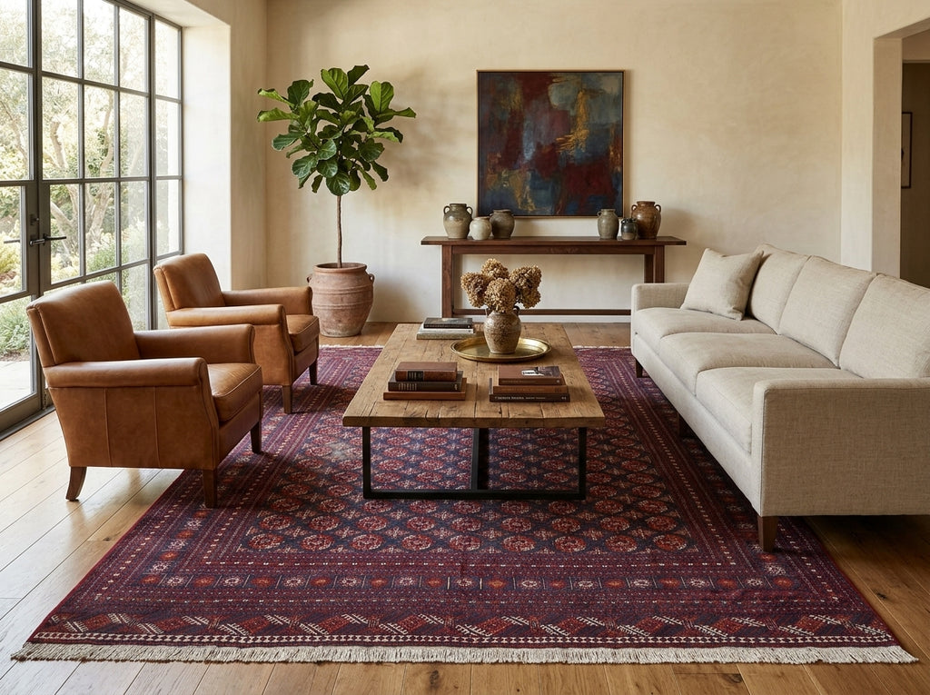 A styled living room featuring a large traditional Persian-style area rug in deep red and navy tones, with a wooden coffee table, a cream-colored sofa, two brown leather armchairs, and a potted fiddle-leaf fig plant.