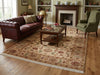 Load image into Gallery viewer, A large traditional area rug with a floral pattern and cream fringe, styled in a classic living room setting with a dark brown leather sofa, wooden coffee table, and fireplace.