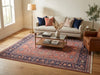 Load image into Gallery viewer, A large traditional Persian-style area rug with a red, navy, and beige pattern, styled in a bright living room under a light gray sofa and a glass-top coffee table.